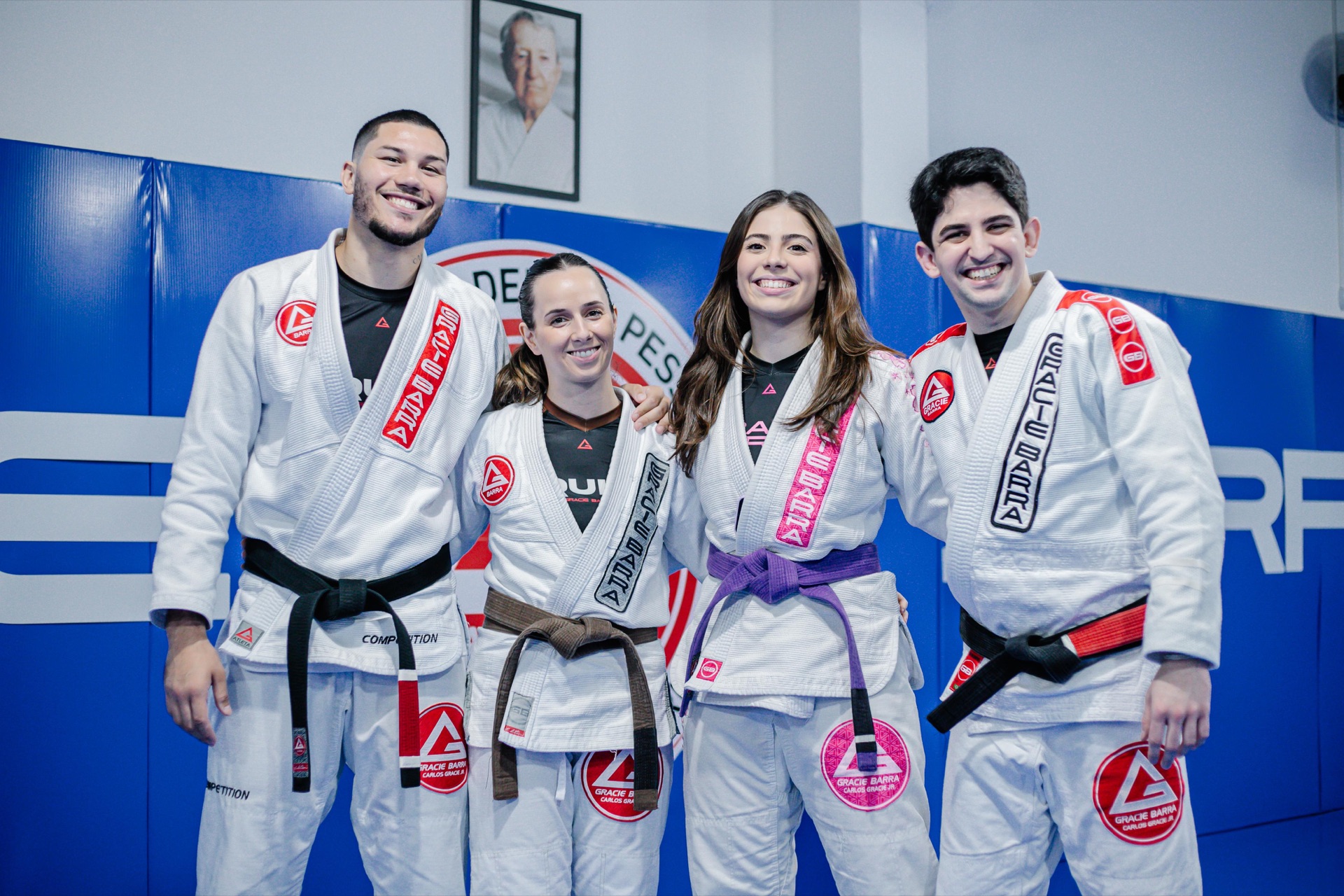 Os quatro instrutores da Gracie Barra Tubarão lado a lado no tatame, sorrindo: Professor Arion, Instrutora Glaucia, Instrutora Julia e Professor Lucas