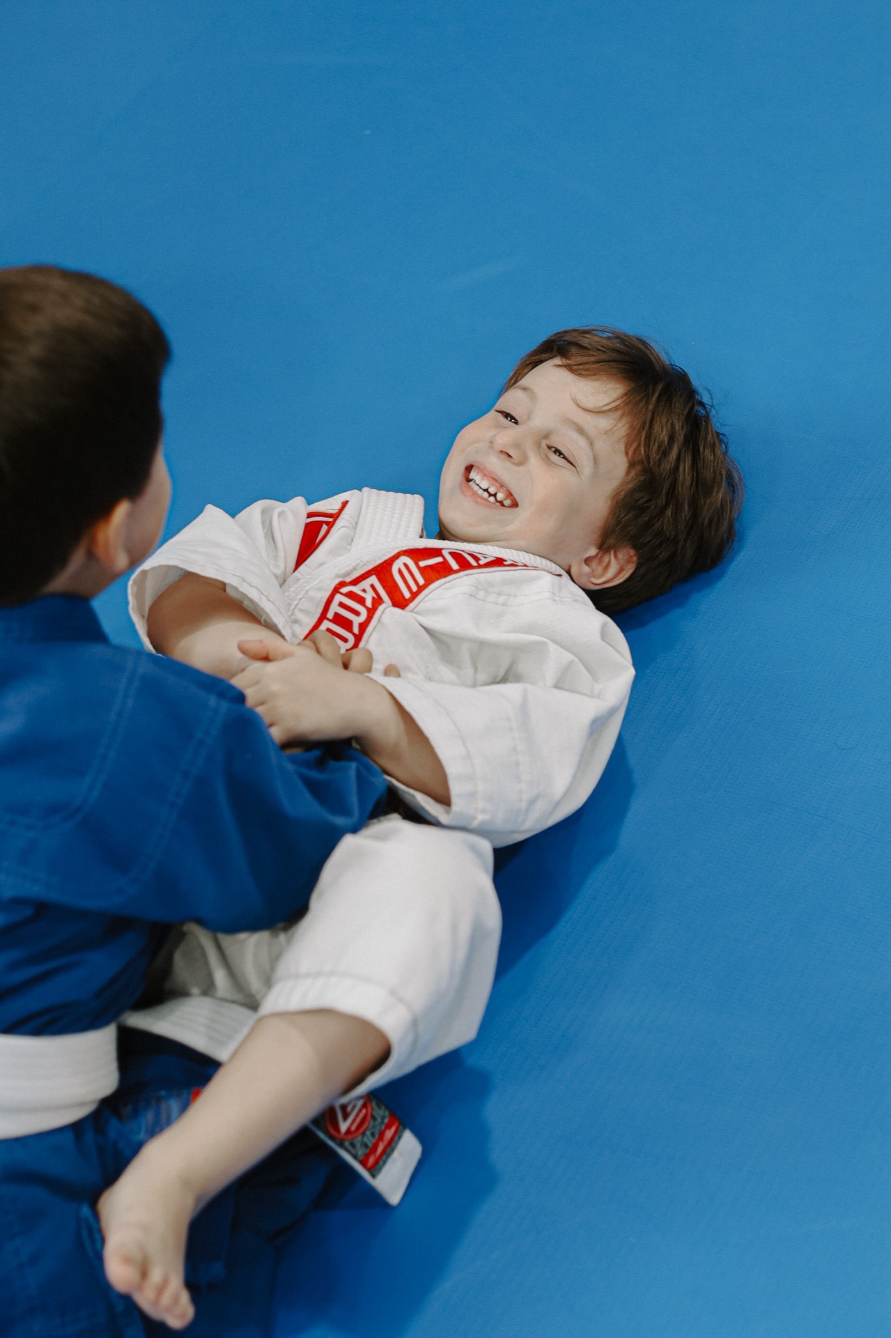 Duas crianças de kimono rindo enquanto treinam no tatame azul