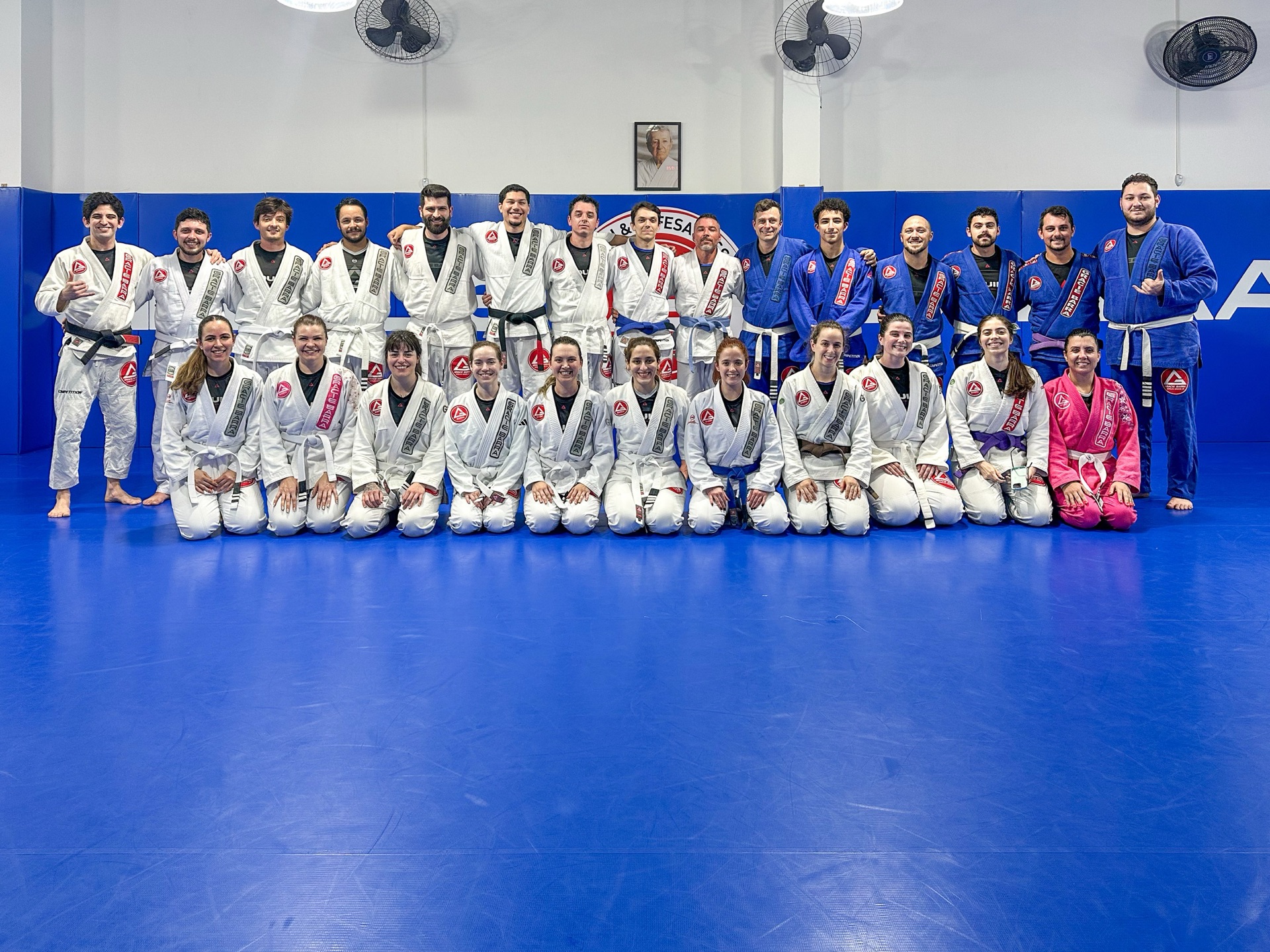 Equipe de instrutores e alunos da Gracie Barra Tubarão posando lado a lado no tatame azul